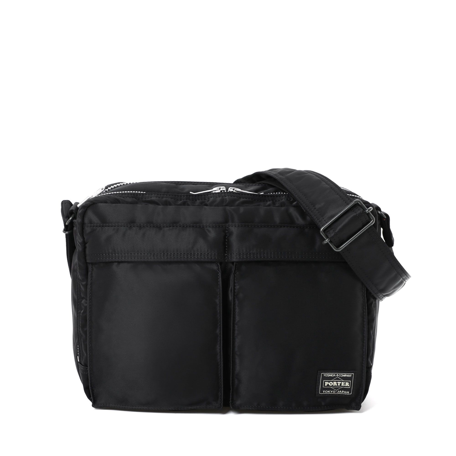 Black nylon sling bag with two front pockets, a top zipper, a shoulder strap, and a small brand label.