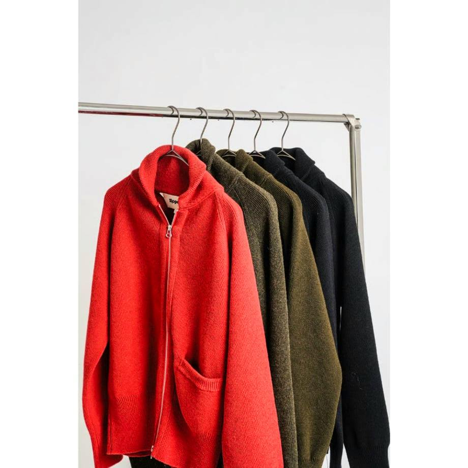A red wool women's jacket with a zipper and pocket hanging on a clothing rack alongside other jackets.