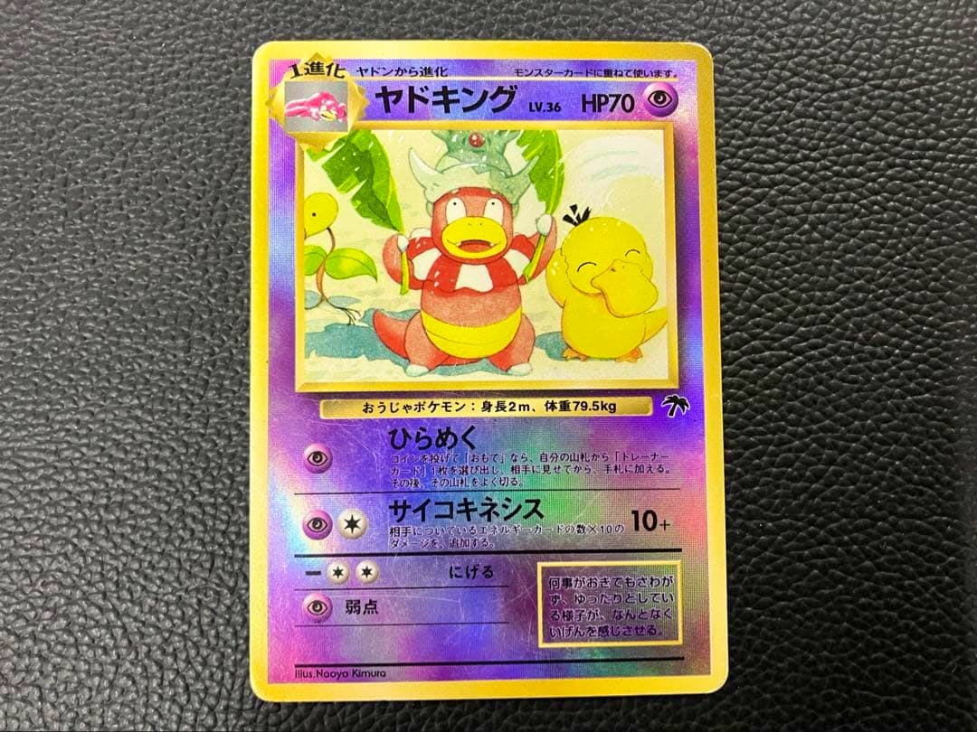 Photograph of the front of a holographic ヤドキング trading card placed on a black textured background.