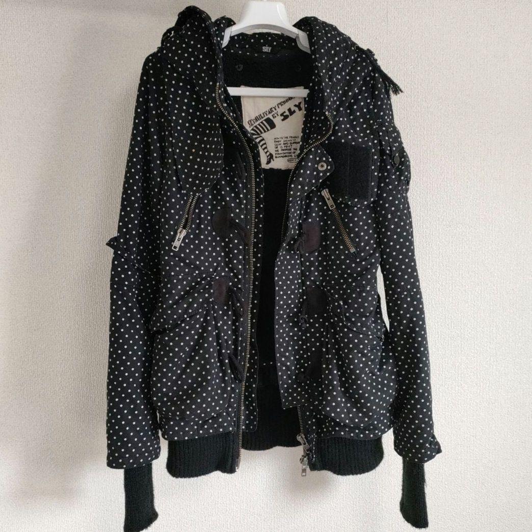 Front view of a black polka-dot women's short jacket with a hood, zipper, and long knit cuffs hanging on a hanger.
