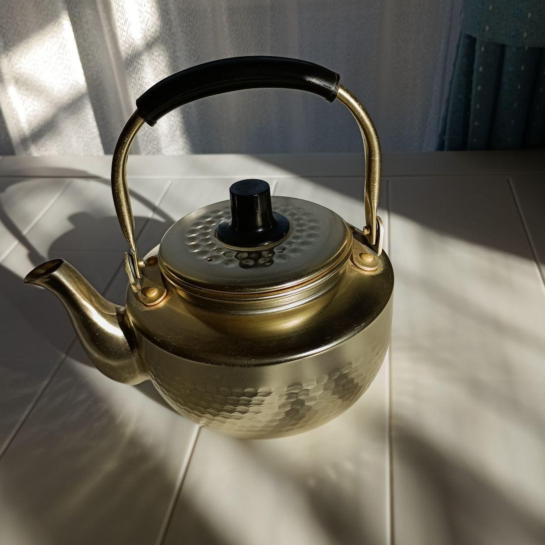 Small anodized aluminum teapot on a table, showing the handle, lid, and spout.