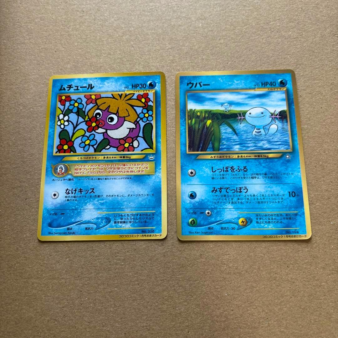Two Japanese promotional trading cards (ムチュール and ウパー) shown side by side on a brown surface.