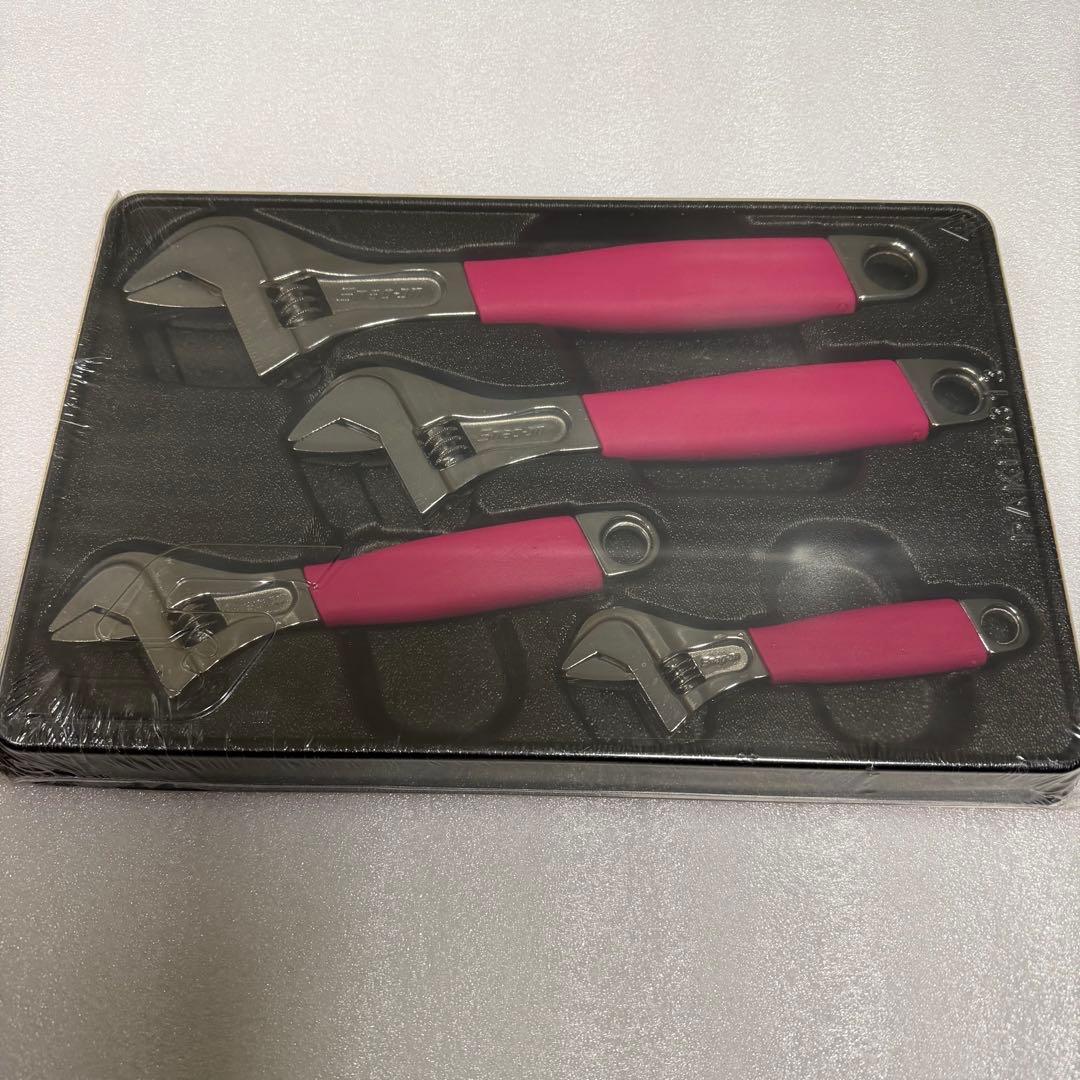 Four pink-handled metal adjustable wrenches displayed in a black molded tray in their packaging.