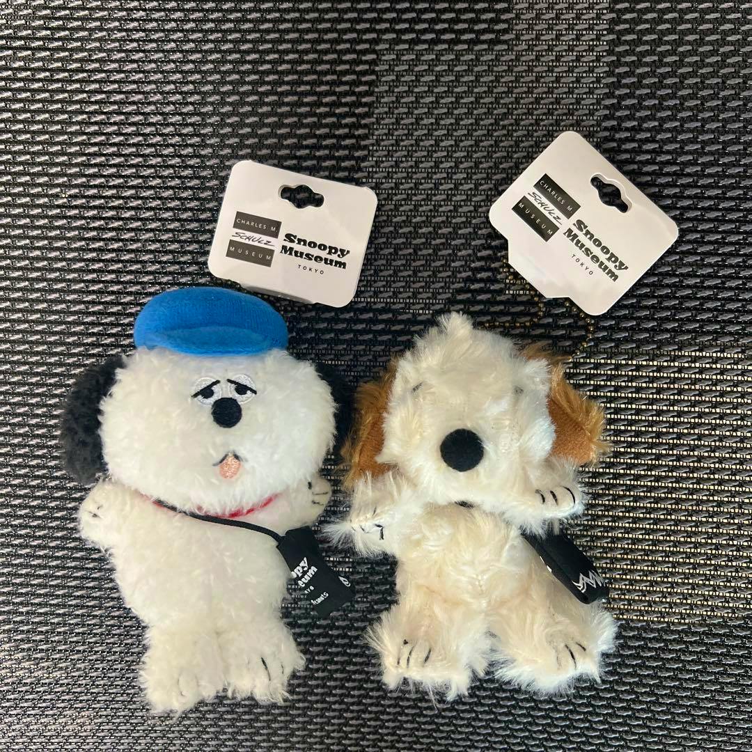 Two small Snoopy Museum plush keychain toys shown side by side on a textured background with their attached tags.