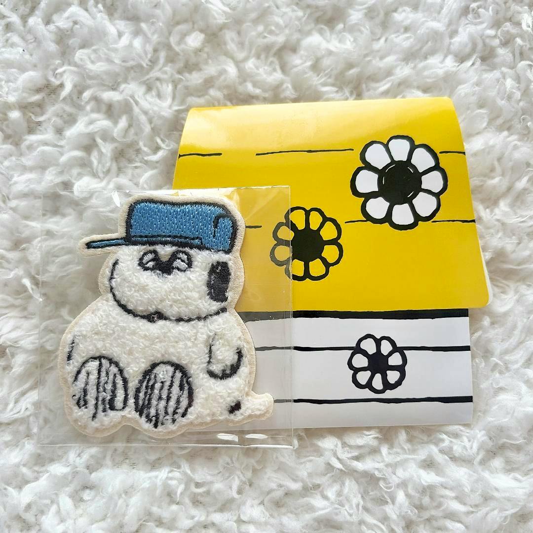Embroidered Snoopy sticker patch with a blue cap in plastic packaging on a fluffy white background and a yellow floral backing card.