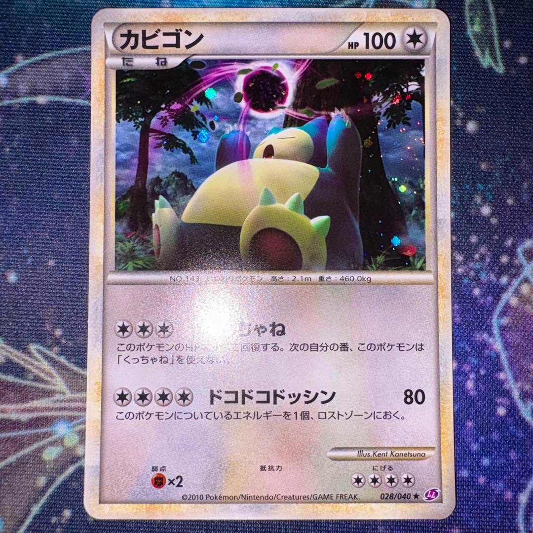 Front of the カビゴン (Snorlax) trading card 028/040 showing the holographic artwork and Japanese text on a playmat background.