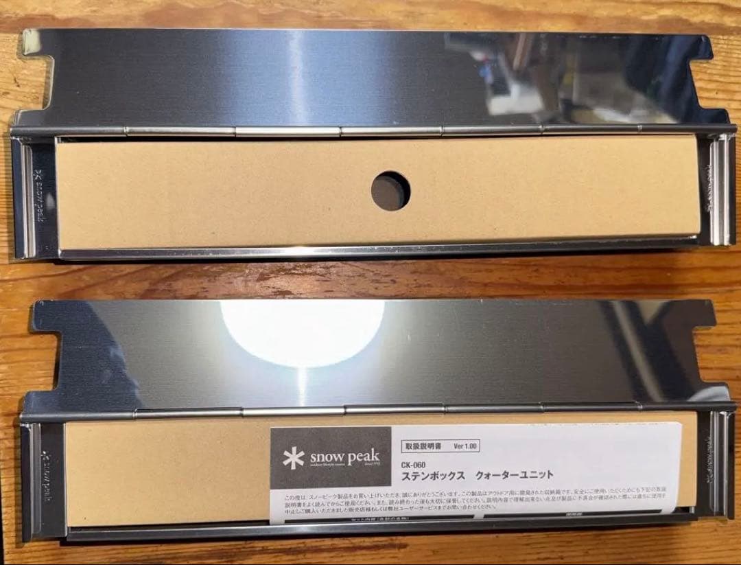 Two stainless Snow Peak ステンボックス クォーターユニット metal parts with cardboard inserts shown on a wooden surface.