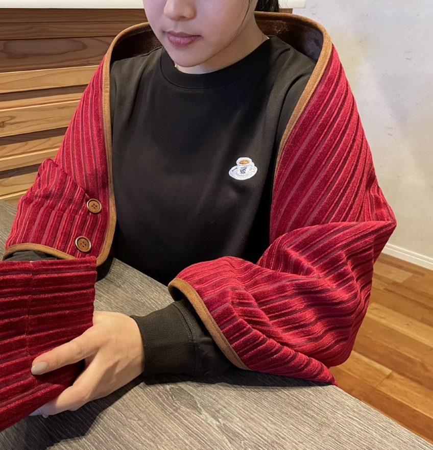 A person seated at a table wearing a red striped blanket draped over their shoulders.