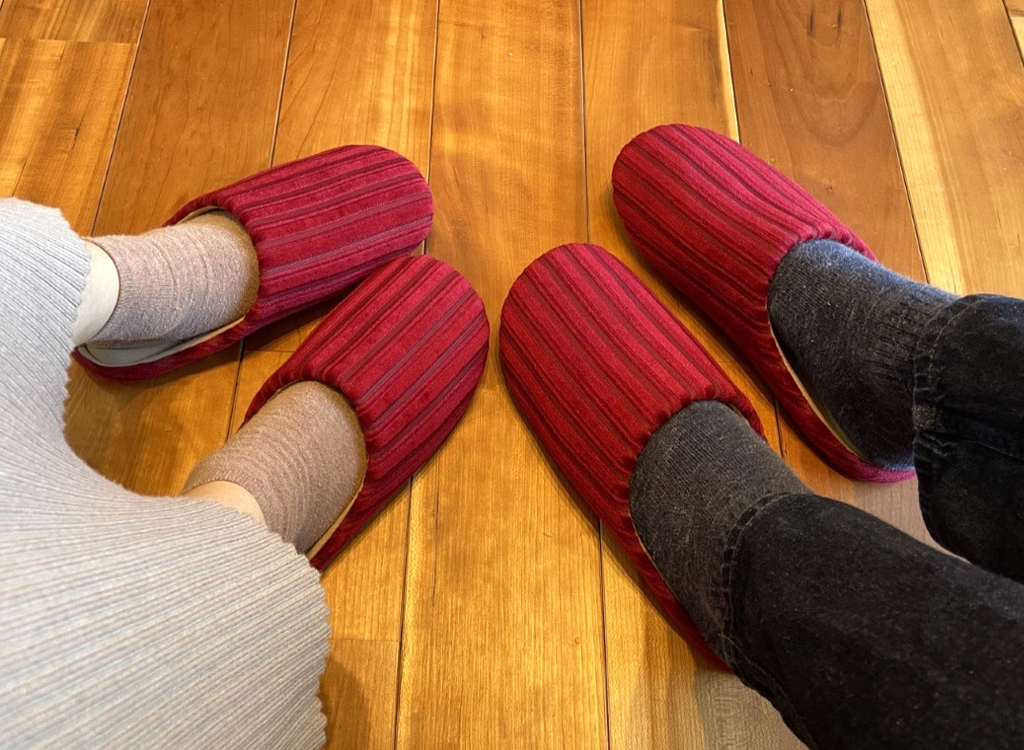 Two people wearing red striped room slippers seated on a wooden floor.