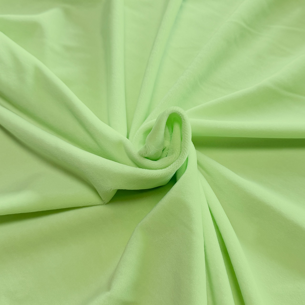 Light green short-pile polyester fabric for plushies, shown draped and twisted to display texture.