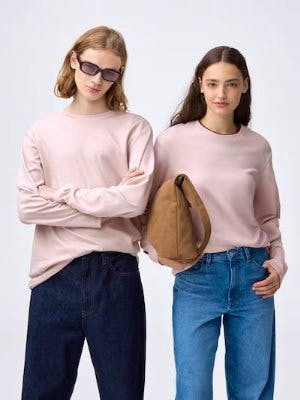 Two models wearing pink long-sleeve crew-neck cotton T-shirts, one holding a brown bag.