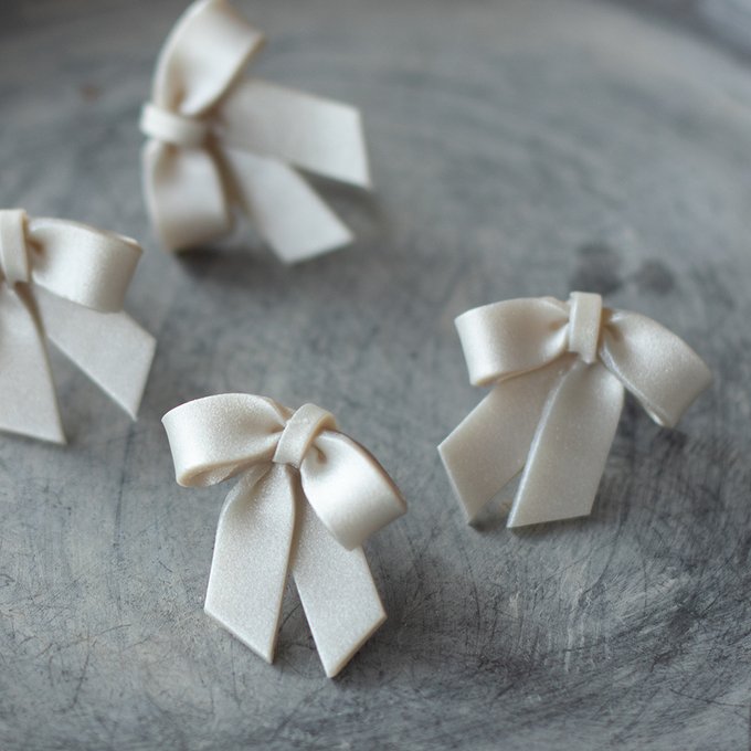 Pearl-white ribbon earrings displayed on a textured surface.