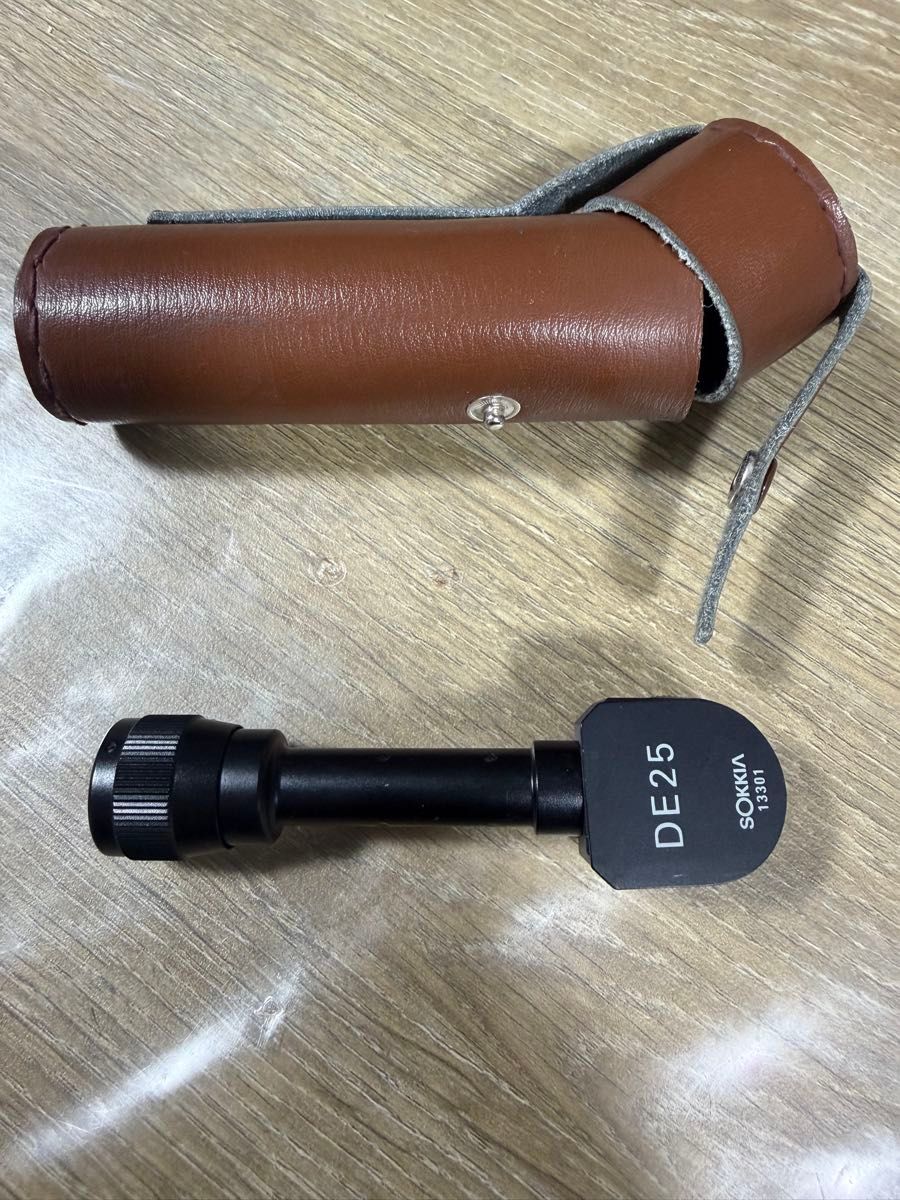 Sokkia diagonal eyepiece DE25 next to a brown leather carrying case on a wooden surface.
