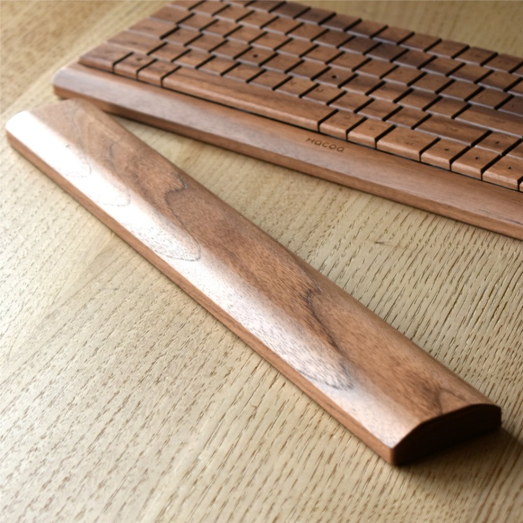 A cherry wood palm rest for a keyboard placed on a wooden desk with a keyboard visible behind it.