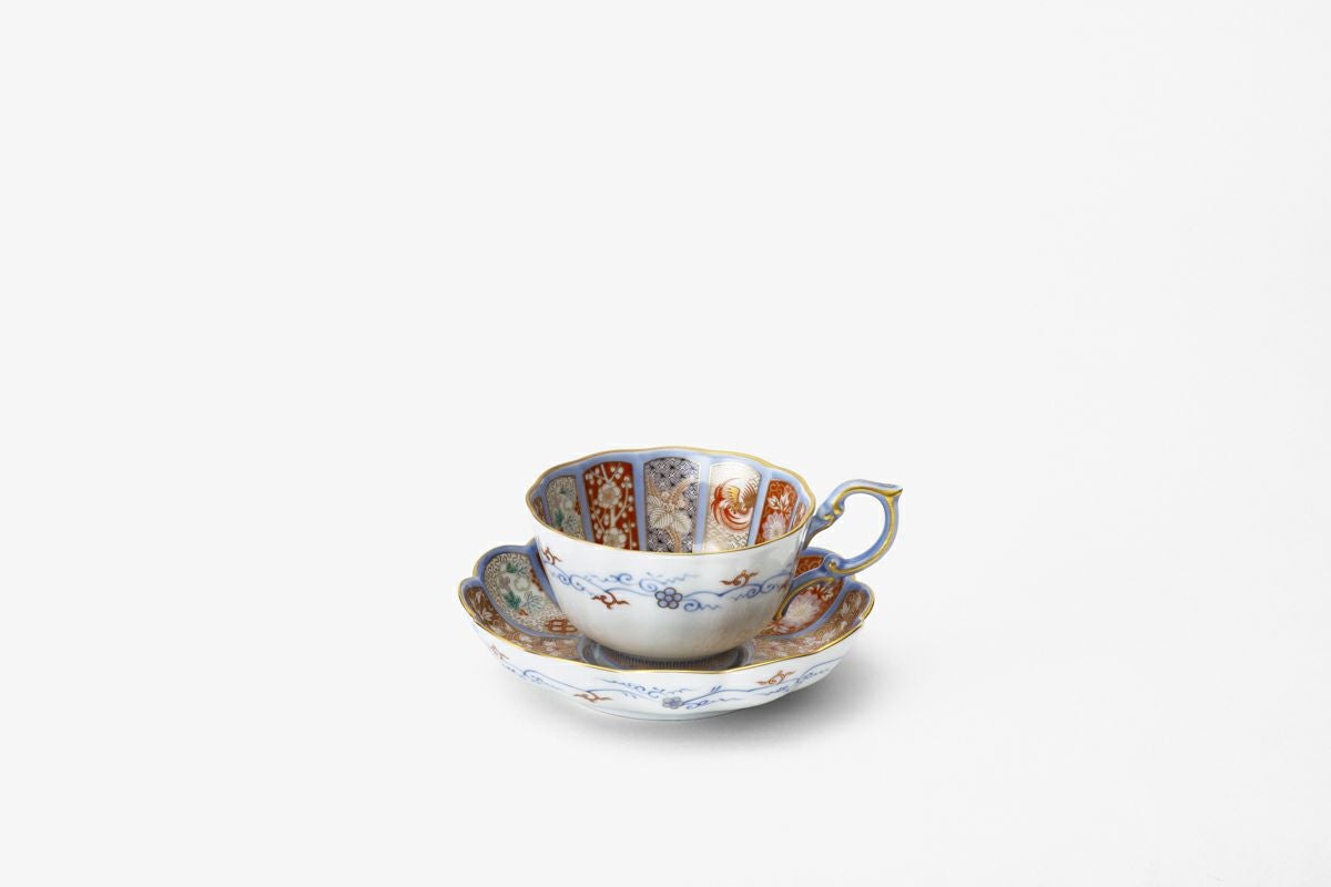 Porcelain teacup and saucer with multicolored decorative panels and gold accents on a white background.