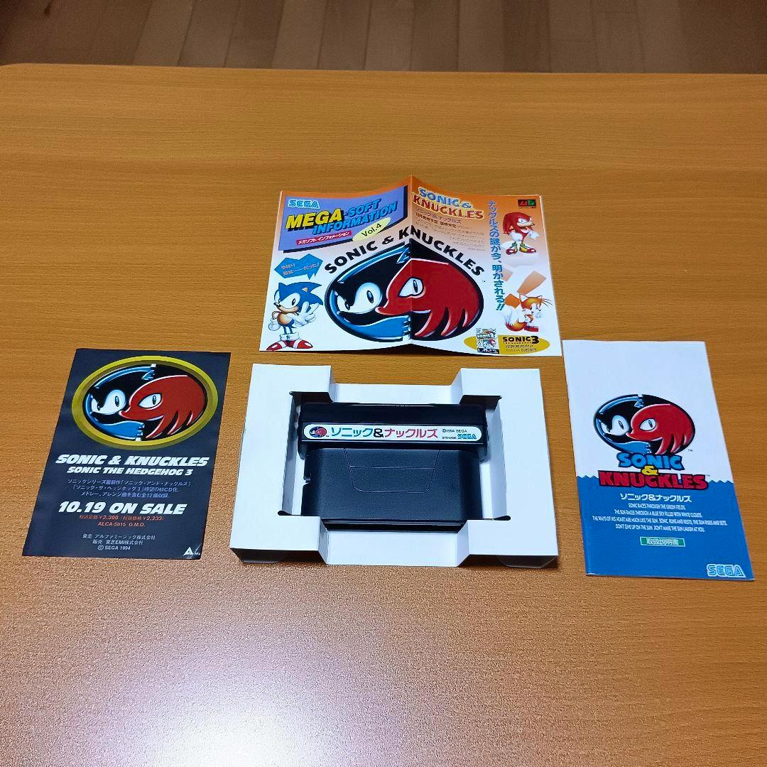 A Sonic & Knuckles Mega Drive cartridge in its white cardboard tray with accompanying flyers and inserts arranged on a wooden surface.