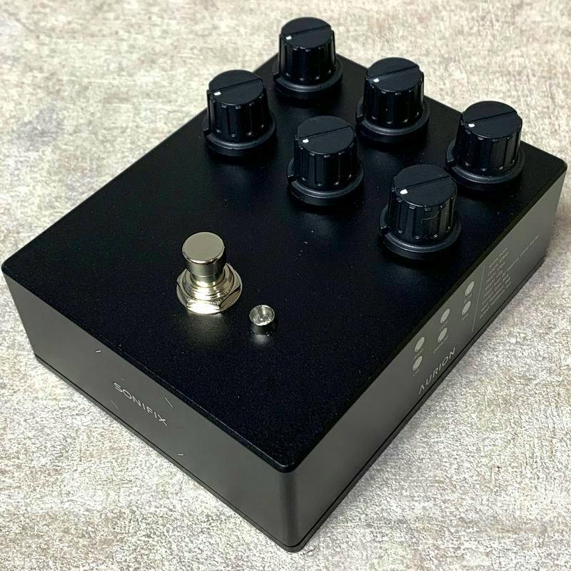 Black SONIFIX AURION bass overdrive pedal on a fabric surface showing multiple control knobs, a footswitch, and a small LED.