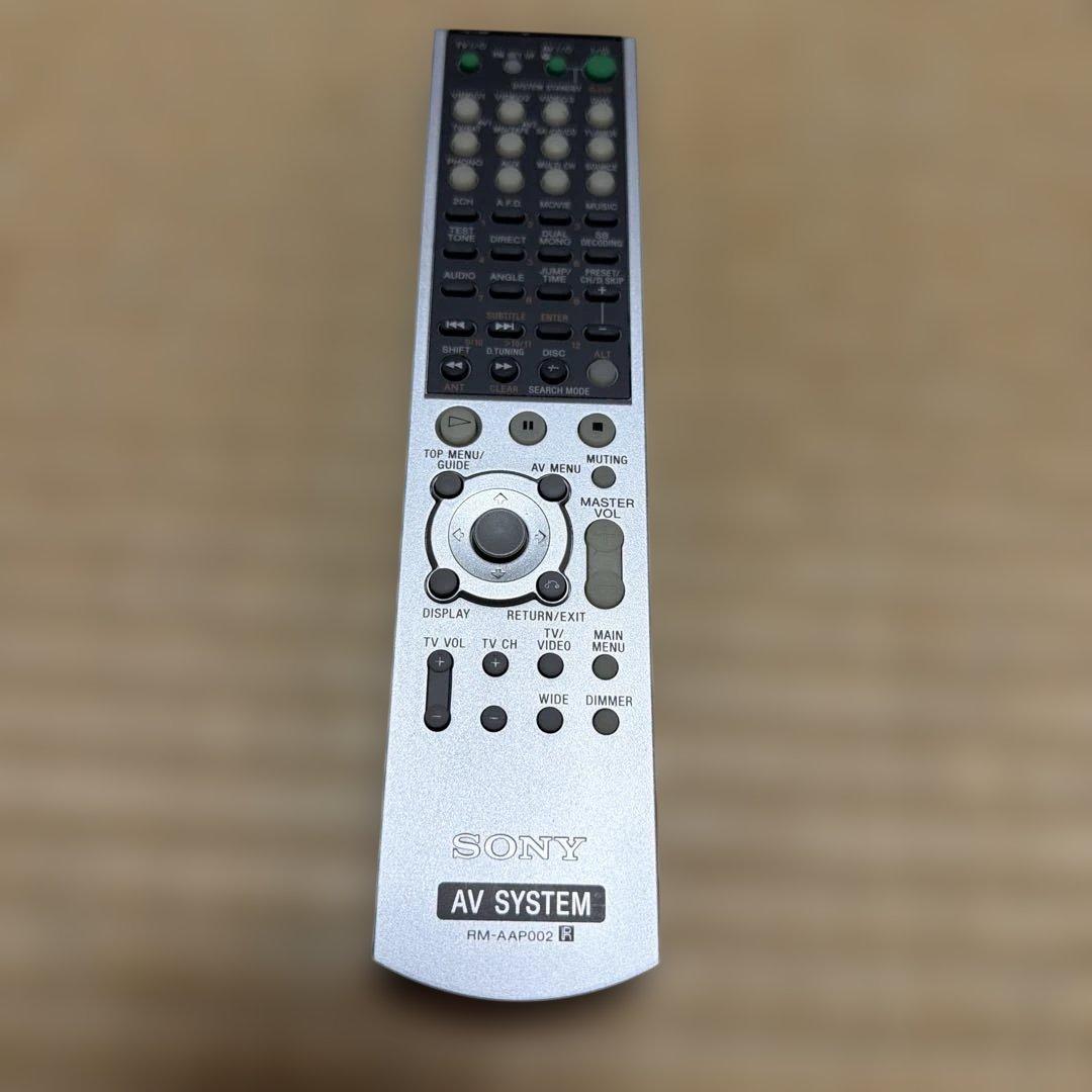 Silver Sony AV amplifier remote control RM-AAP002 photographed from above on a wooden surface showing the front face and buttons.