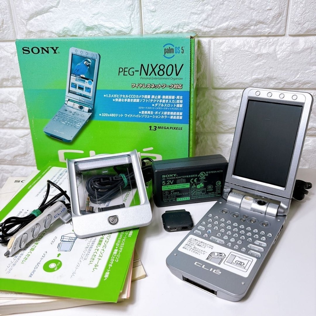 Open Sony CLIE PEG-NX80V PDA shown with its original box, charger, cradle, and cables visible beside it.