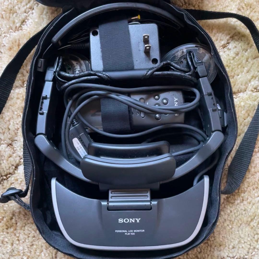 Top-down photo of a SONY PLM-100 personal LCD monitor (Glasstron) headset inside its soft carrying case with attached cables and power adapter.