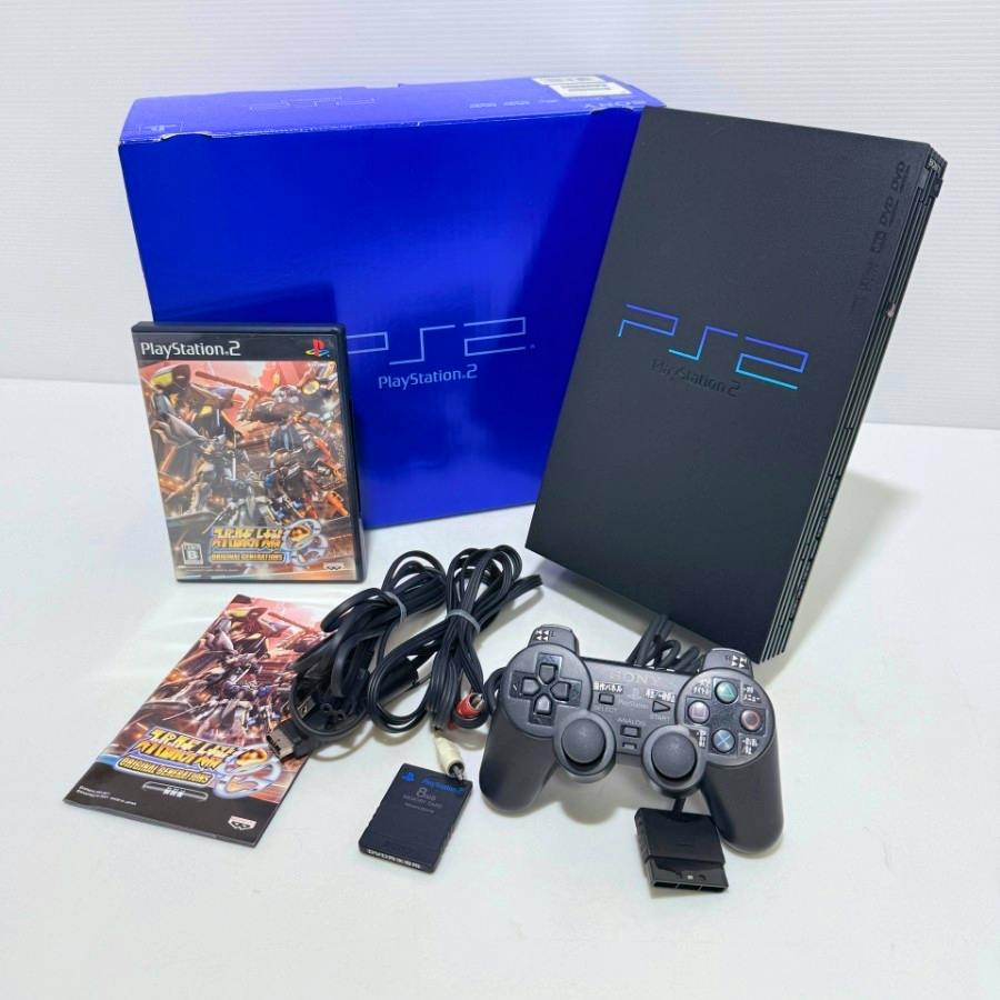 PlayStation 2 console displayed with its blue retail box, controller, cables, memory card, manual, and a PS2 game.