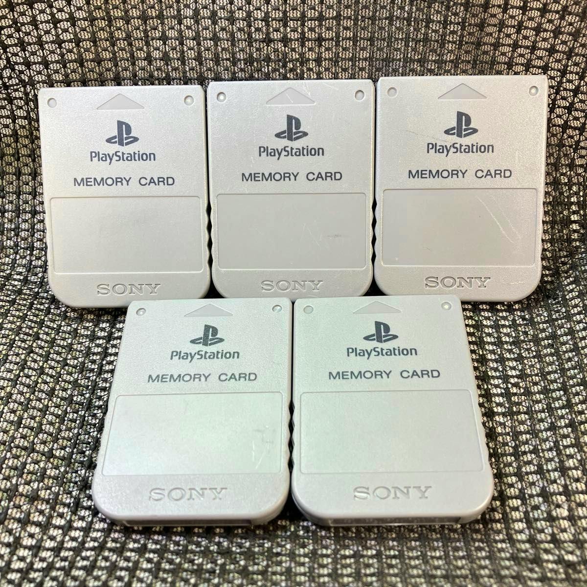 Five silver PlayStation memory cards arranged in two rows on patterned fabric.