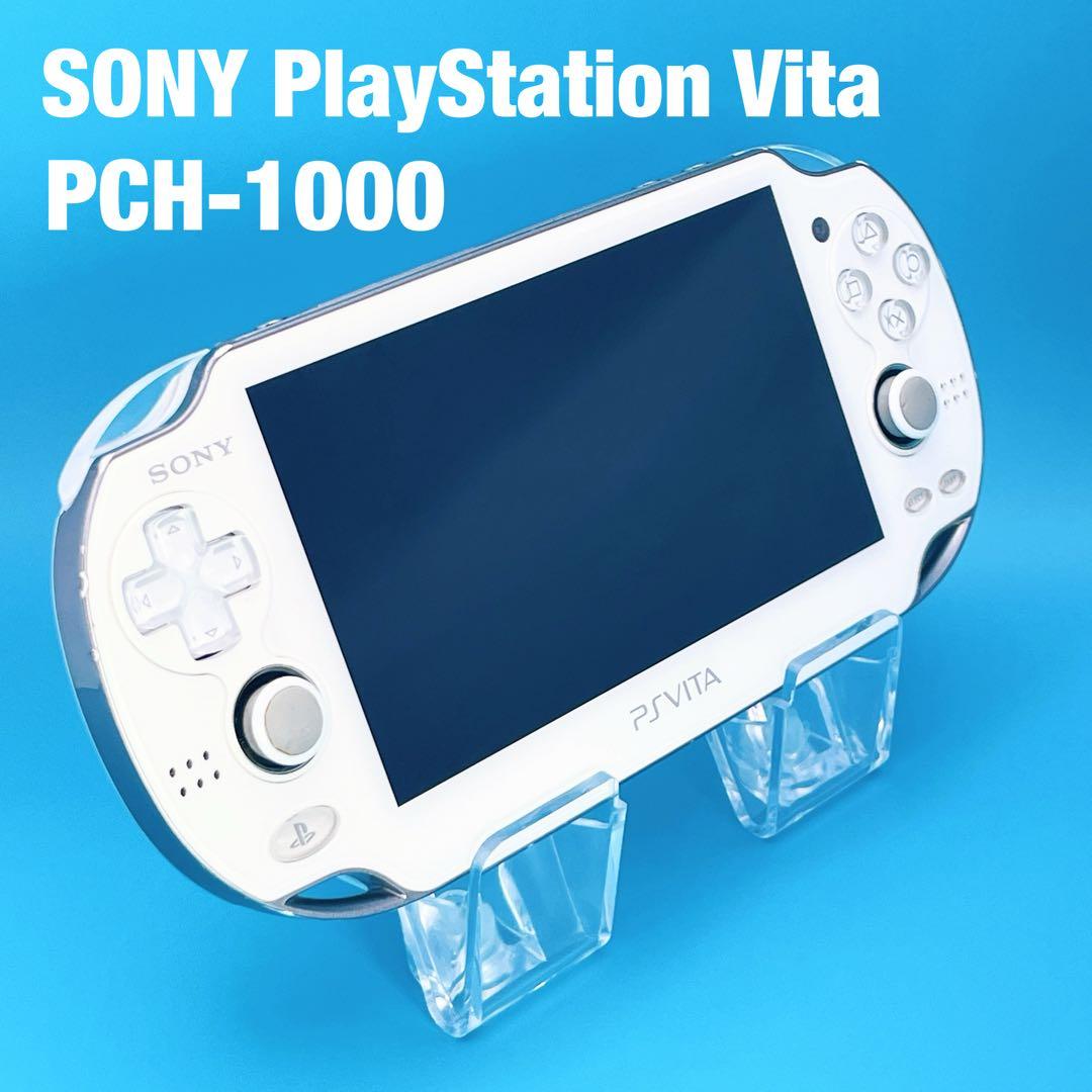 White Sony PlayStation Vita PCH-1000 handheld game console on a clear stand against a blue background.