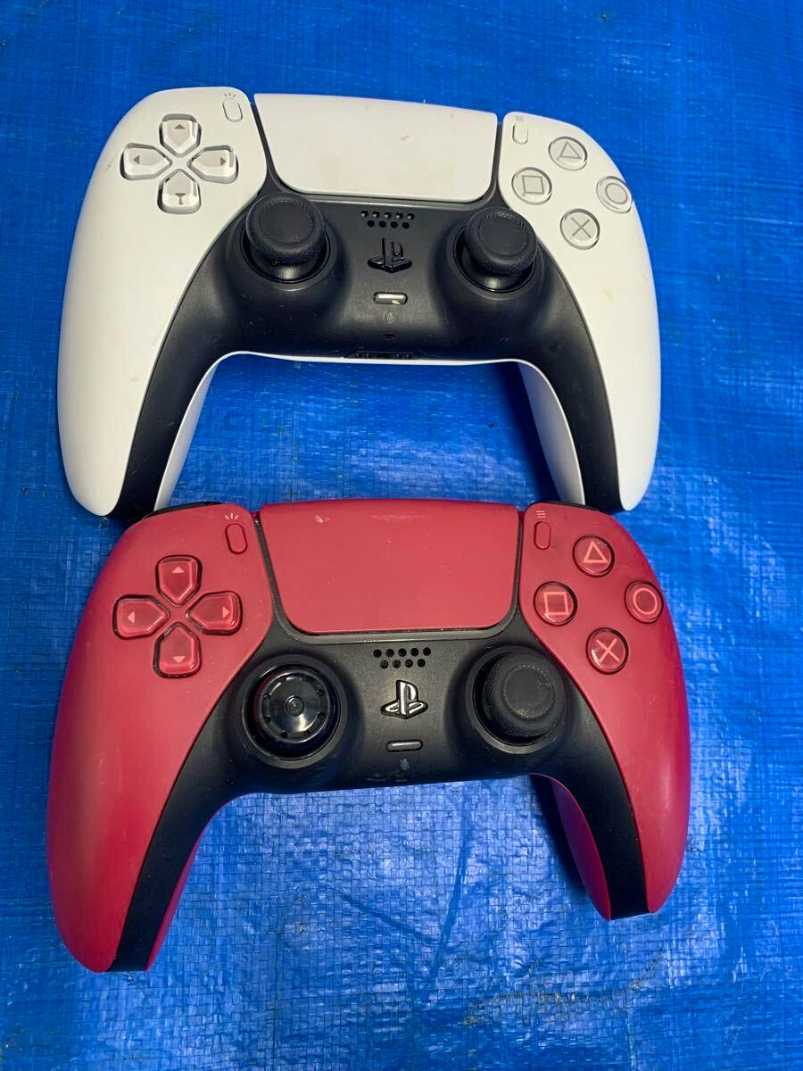 Two used PS5 wireless controllers, one white and one red, shown from the front on a blue surface.