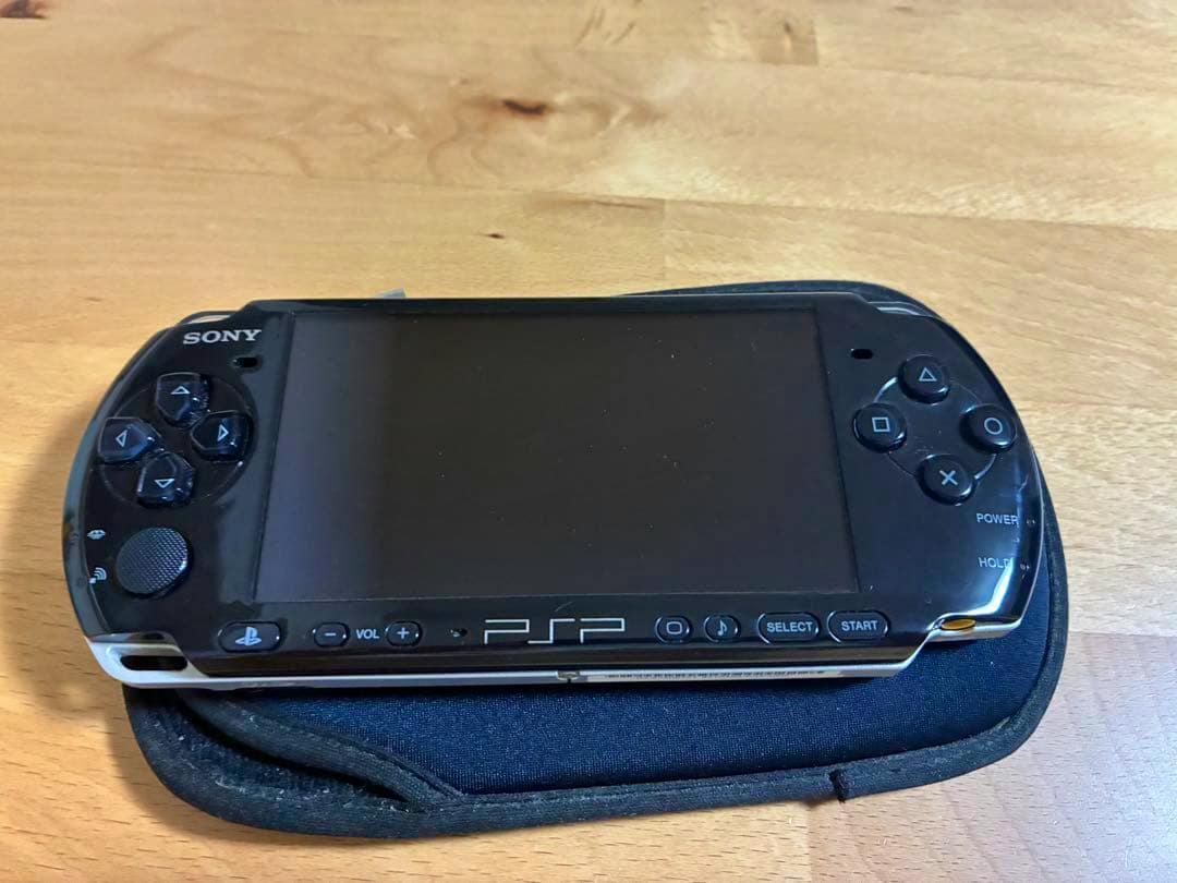 Front view of a black SONY PSP-3000 handheld console showing the screen and buttons resting on a soft case.