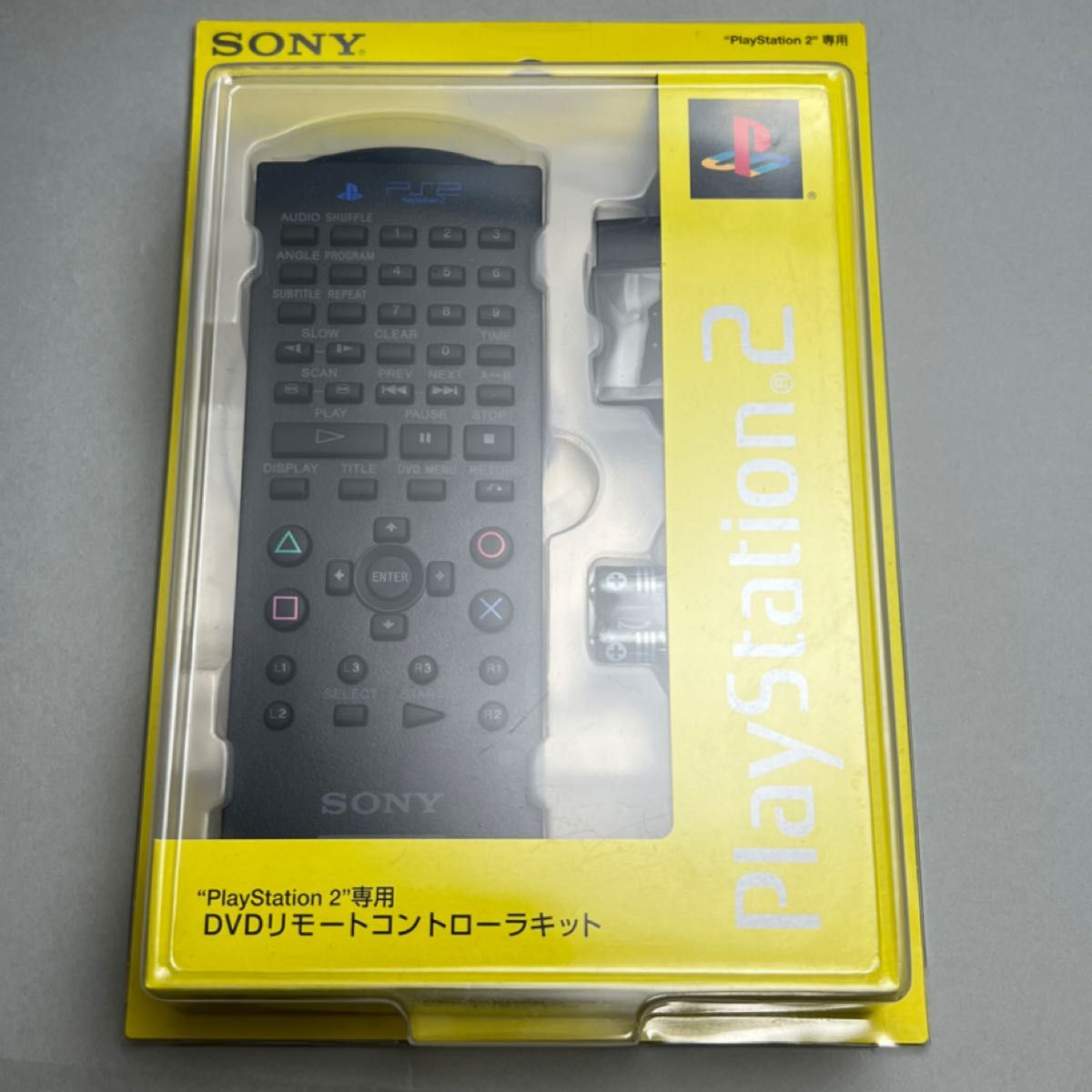 Front view of sealed Sony SCPH-10170 PlayStation 2 DVD remote controller kit in original yellow blister packaging showing the remote and included batteries.