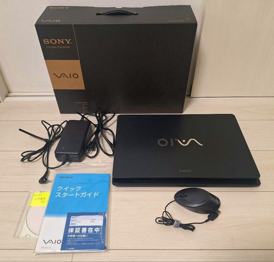 Closed Sony VAIO F-series laptop (VPCF23AJ) with power adapter, USB mouse, manuals, and the original Sony VAIO box arranged on a light wood floor.