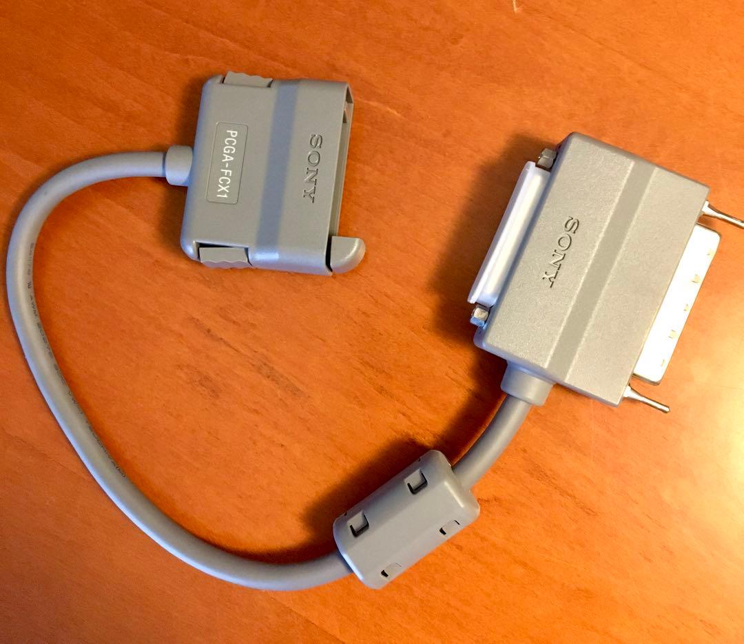 Gray Sony VAIO PCGA-FCX1 cable adapter with two connectors laid on a wooden surface.