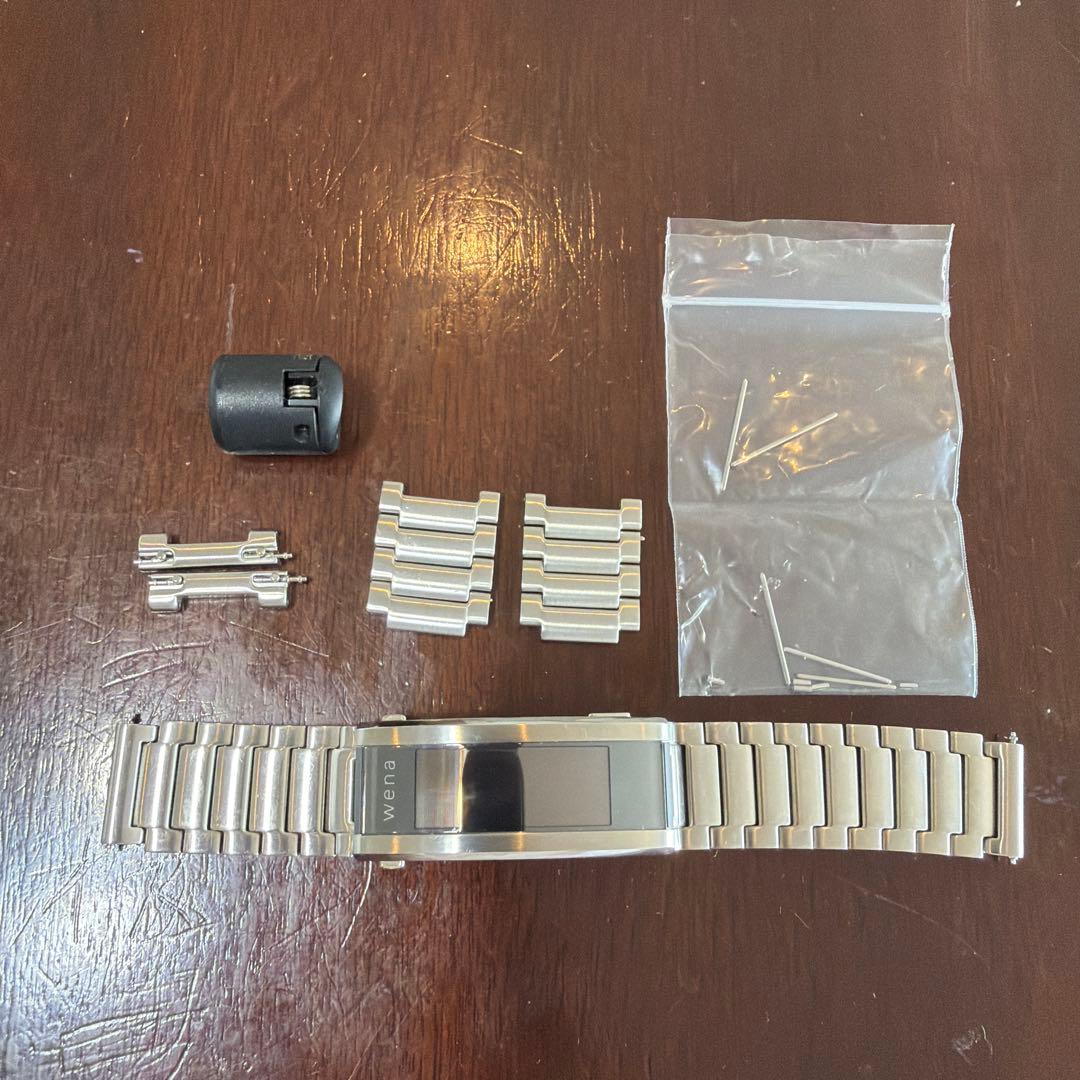 Silver Sony wena metal watch band with spare links, 20mm adapters, pins, and a small black tool laid out on a wooden surface.