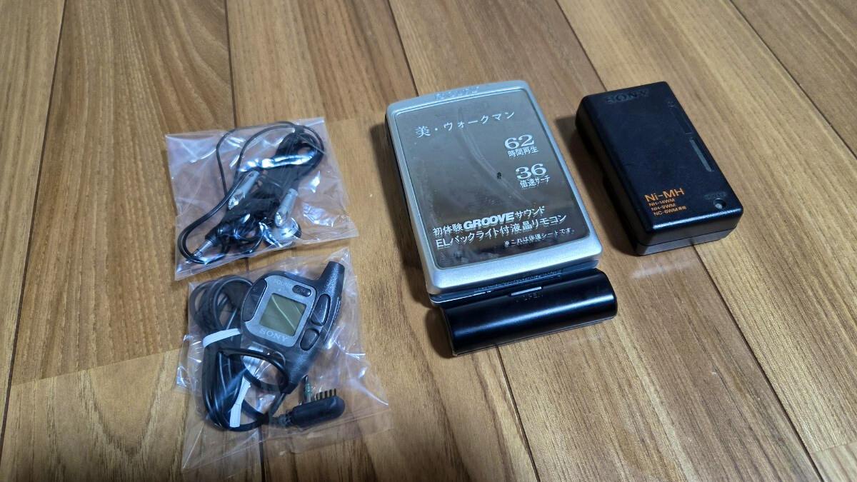 Sony WM-EX5 Walkman cassette player with a battery pack, remote control, and earphones laid out on a wooden floor.
