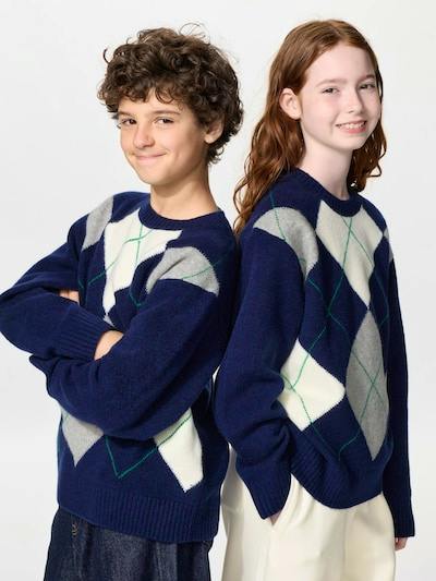 Two young models wearing navy argyle crewneck sweaters posed back-to-back.