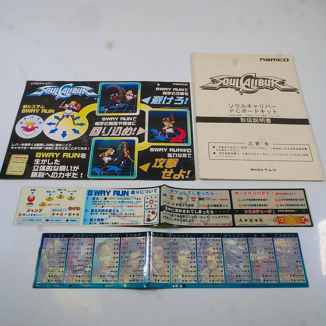 Flat lay photo showing a SoulCalibur poster, the SoulCalibur instruction manual, and two long printed obi strips on a white surface.