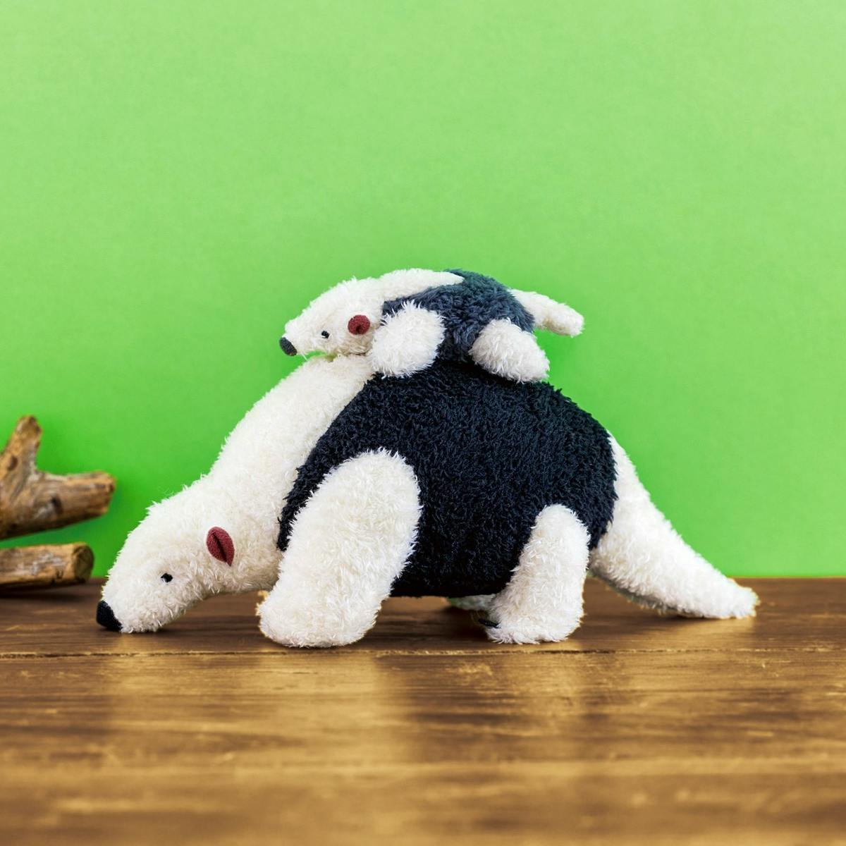Plush parent-and-baby southern tamandua pouch displayed on a wooden surface with a green background.