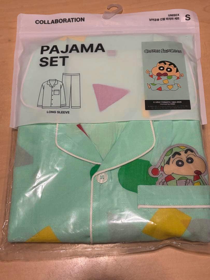 Folded long-sleeve Crayon Shin-chan pajama set in clear retail packaging showing mint-green fabric, piped collar, and a printed character on the pocket.