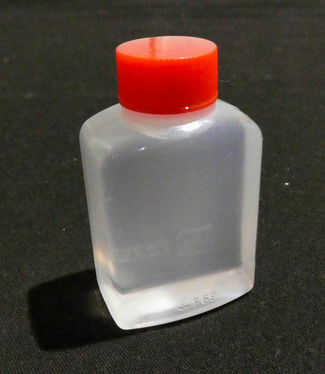 A small translucent plastic bottle of sword oil with a red cap sitting on a black background.
