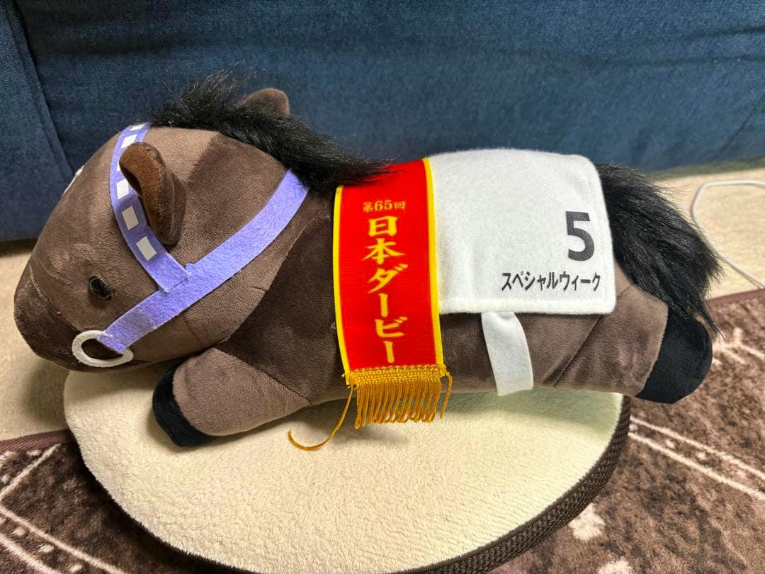 A Special Week plush toy for the 65th Japan Derby lying on its side showing the red sash and white number 5 on its blanket.