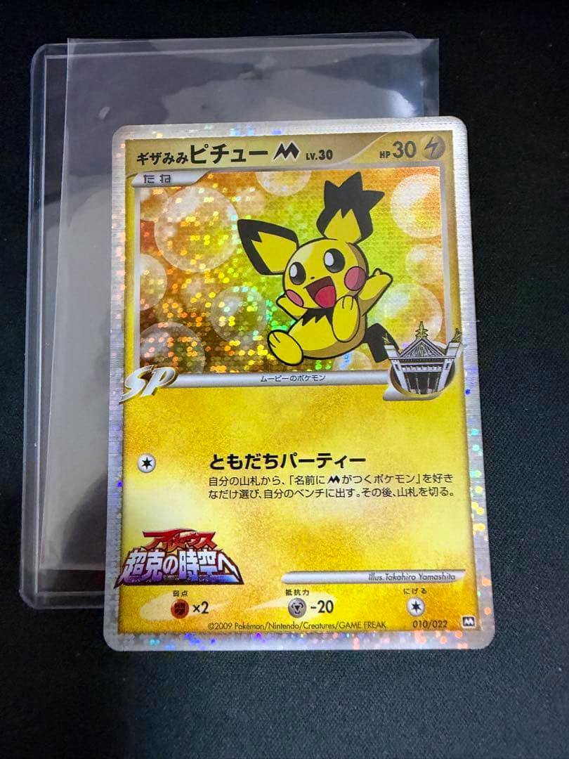 Holographic ギザみみピチュー M trading card (010/022) shown in a clear sleeve on a dark surface.