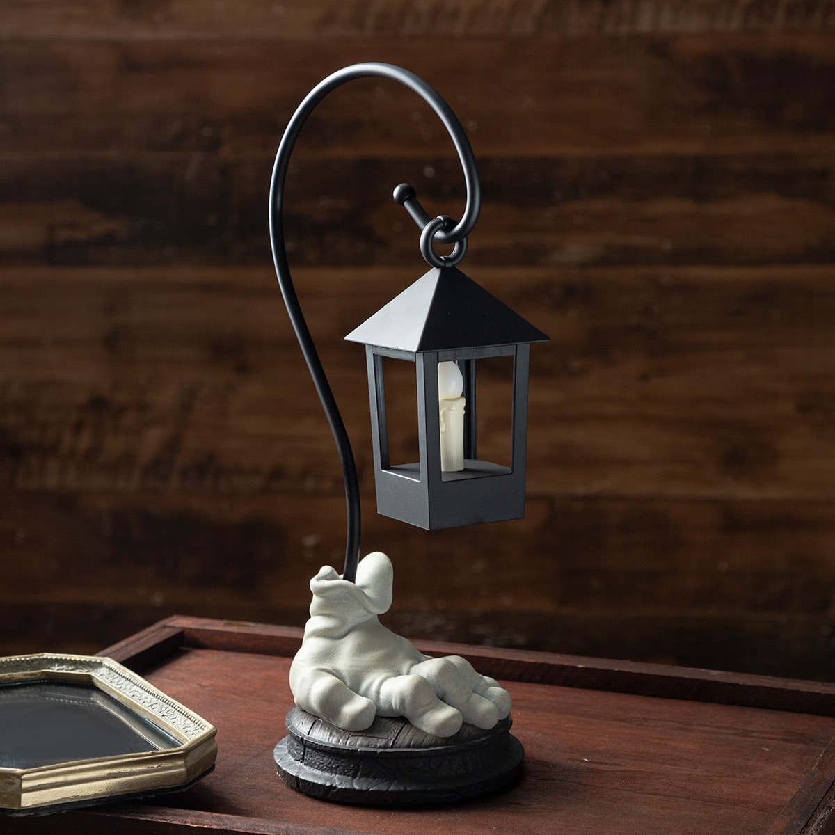 LED table lamp showing a hanging lantern above a sculpted white hand base on a wooden surface.