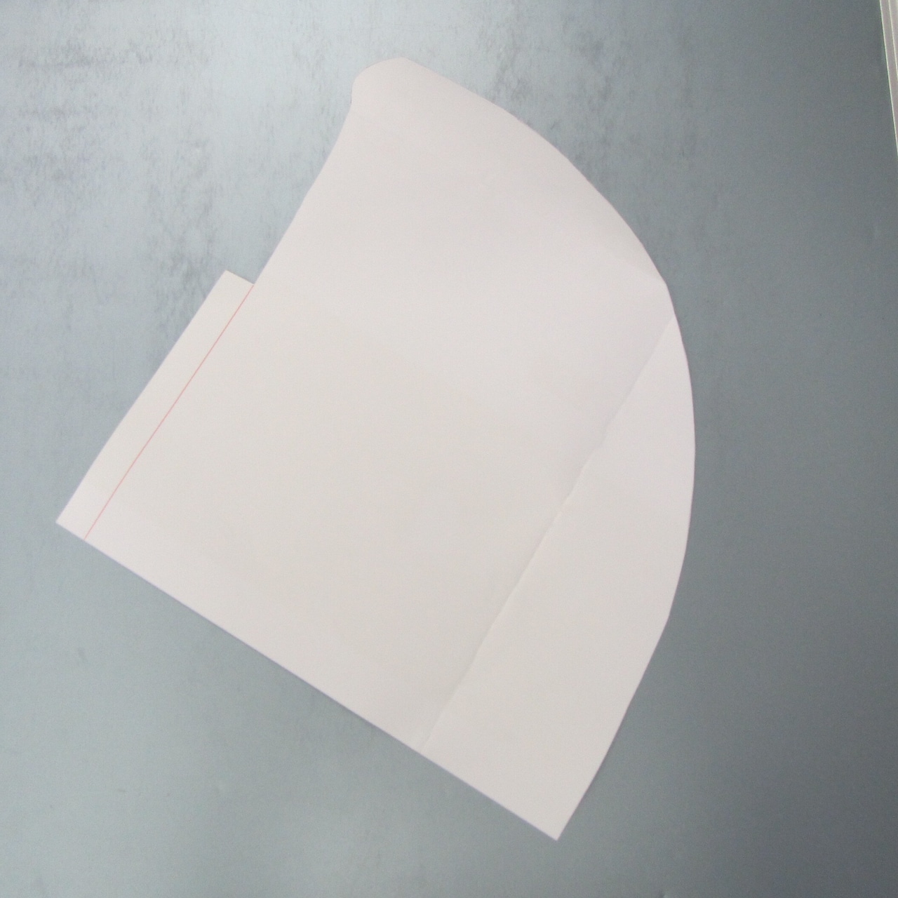 A paper pattern piece for an eboshi (hat) laid flat on a gray surface.