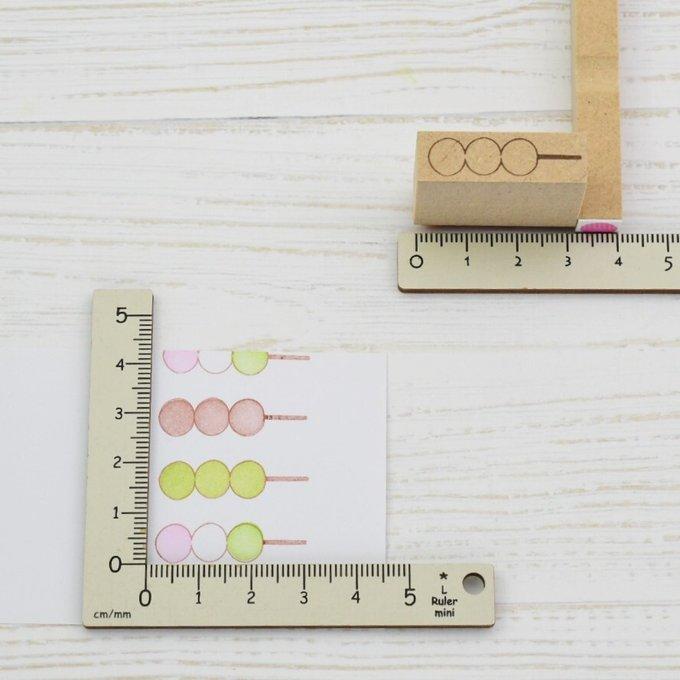 A wooden stamp for a three-ball dango skewer beside rulers and stamped impressions on paper.