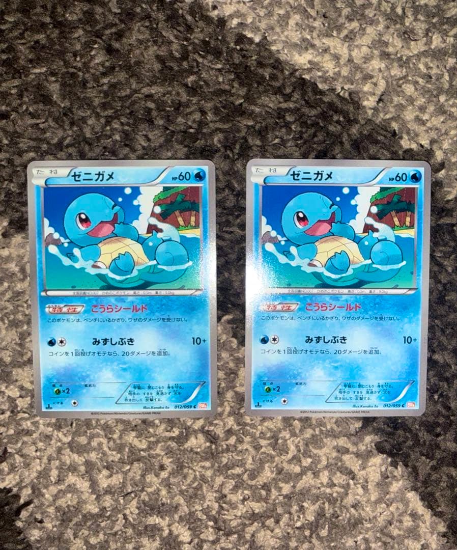 Two front-facing Japanese Squirtle (ゼニガメ) Pokémon trading cards shown side-by-side on a carpeted background.