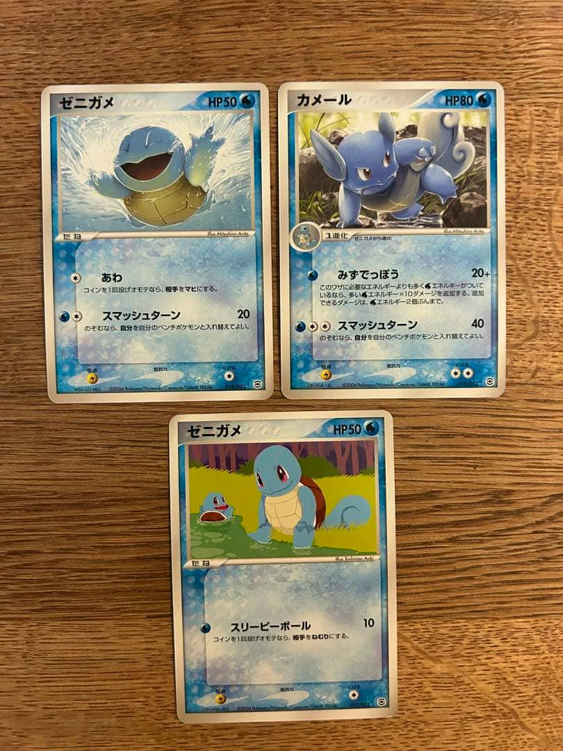 Three trading cards (ゼニガメ and カメール) arranged on a wooden surface.