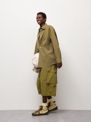 Male model wearing olive-green baggy cropped men's pants with a matching shirt and sneakers.