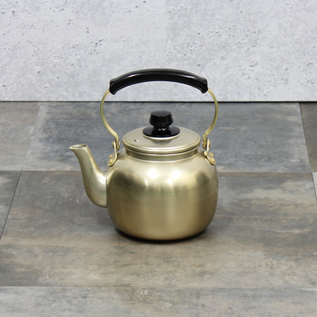A stainless steel kettle-style pot with spout, lid, and black handle placed on a tiled surface.