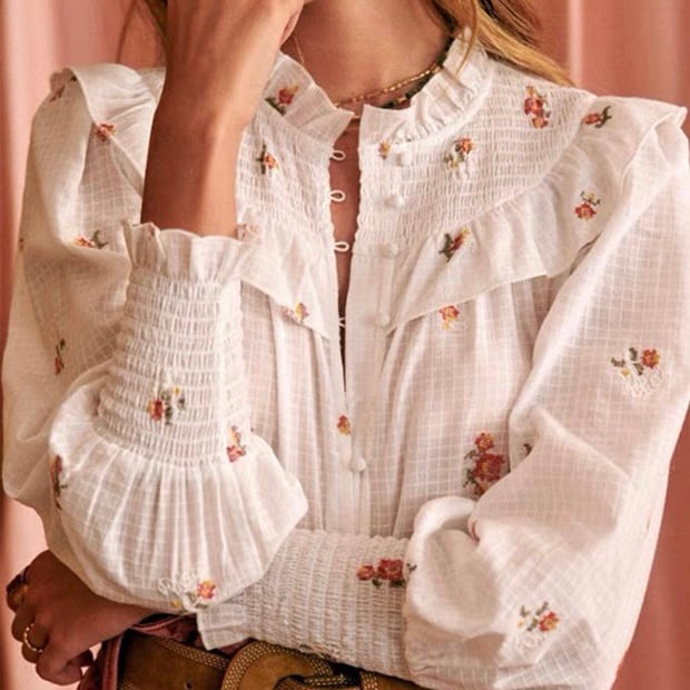 White stand-collar women's blouse with small floral embroidery, puff sleeves, smocked cuffs, and front buttons, shown on a model.