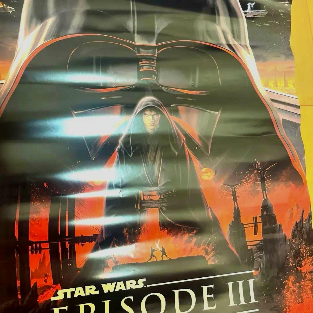 Photograph of a Star Wars Episode III (Revenge of the Sith) poster showing a large Darth Vader helmet silhouette with a hooded Anakin in front and a fiery duel scene below.